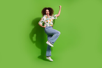 Full length photo of excited lucky lady wear print shirt rising fists jumping high empty space isolated green color background