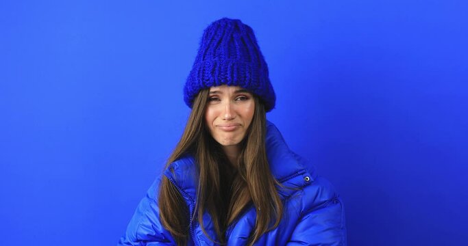 Perplexed dissatisfied woman looks frustrated at camera says I don't agree has puzzled face expression dressed blue puffer jacket isolated over blue background. Girl shake her head. No, deny.