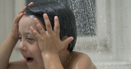 Annoyed child i under shower's cascade, displeased emotion of young boy underneath water flow...