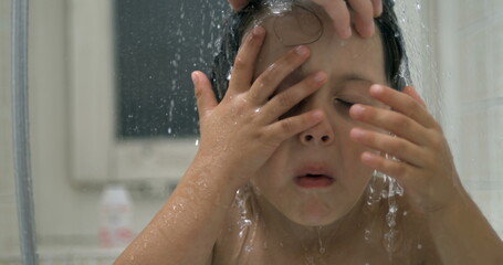 Displeased small boy underneath water shower head while grimacing in annoyance. kid in distress...