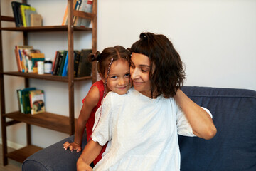 Indoor portrait of two happy people, young mother and her little cute daughter with funny hairstyle...