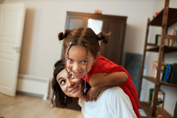 Selective focus on elder sister piggybacking her little one looking at camera with playful facial...