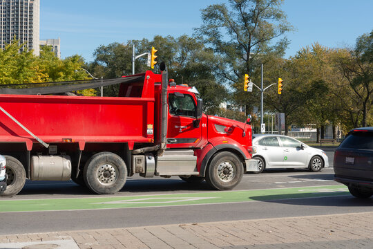 Peterbilt Motors Company 567 red dump truck with tarp netting on the street at a signalized intersection in autumn