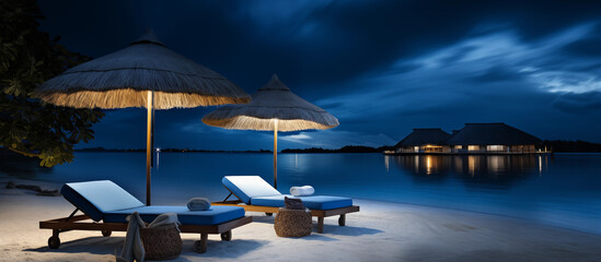 Fototapeta na wymiar Beach lounger and straw umbrella at night. Blue palm tree beach umbrella and chaise lounge chair. An overnight resort on an oceanfront island. Sandy beach paradise vacation under the stars