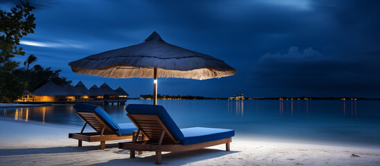 Beach lounger and straw umbrella at night. Blue palm tree beach umbrella and chaise lounge chair. An overnight resort on an oceanfront island. Sandy beach paradise vacation under the stars - obrazy, fototapety, plakaty