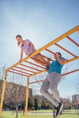 Handsome male sports person doing pull ups in the park while his female friend is doing push ups on horizontal metal bars