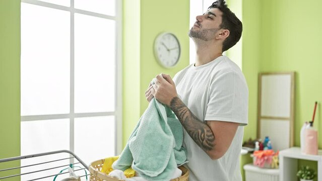 Young hispanic man smelling clean towel at laundry room