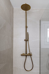 Shower cabin with glass screen, imitation marble tiling and taps with golden shower head