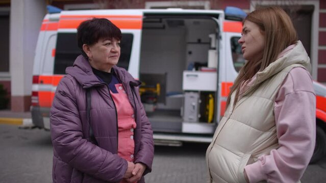 Pregnant woman communicating with paramedic near ambulance