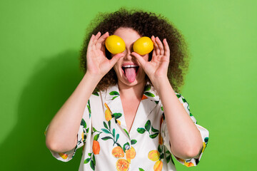 Portrait of excited positive lady arms hold lemons cover eyes show tongue out isolated on green...