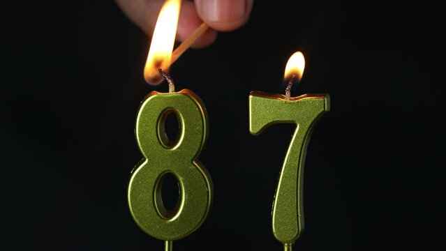 close up on gold number eighty-seventh candle on a dark background.
