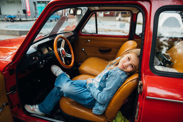 Teenage girl in denim clothes driving a red vintage retro car .