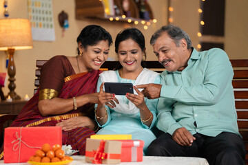 Joyful happy Indian mother and father watching mobile phone with daughter at home during diwali festival celebration - concept of cyberspace, social media sharing and online app streaming