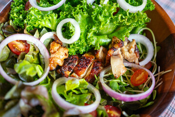 Grilled chicken salad with various type of fresh vegetable, served in wooden bowl and placed on table. Food object photo, selective focus.