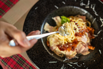 Eating spaghetti carbonara with ham and crispy bacon which is served in black plate. Italian food menu photo. Selective focus.