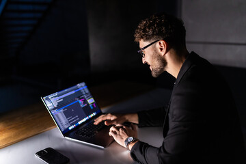 Young smart man mobile developer writes program code on a computer, programmer work in home office.