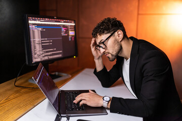 Young smart man mobile developer writes program code on a computer, programmer work in home office.