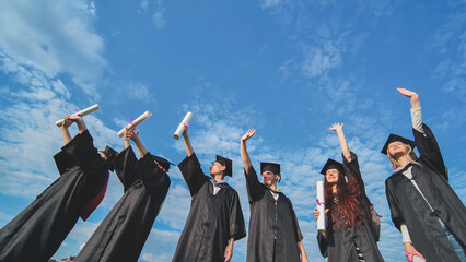 Cheerful graduates waving their diplomas on a sunny day.
