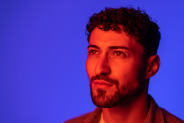 Portrait of young handsome man looking away against gradient purple background in neon light.