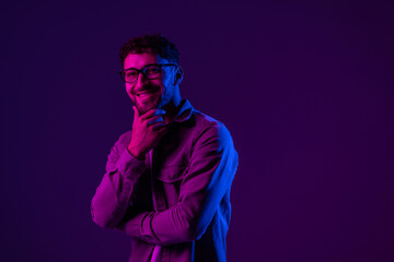 Portrait of smiling man standing looking at camera with confident facial expression on colorful neon light background.