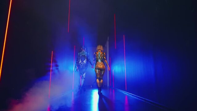 Two women walks studio full smoke, Fantasy cyborg woman robot costume metal human body cyberpunk style hair back rear view. Sexy alien girl in virtual reality game lady warrior future. neon light 4k