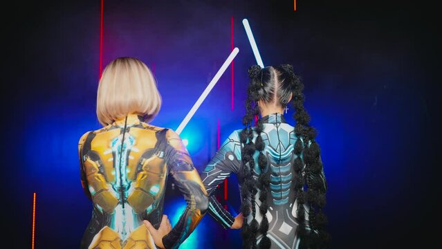 Two women cyborg creative robot costume metal body creative makeup, cyberpunk style blonde hair, braid hairstyle. Sexy alien girl in virtual reality war, woman warrior future vr laser sword in hands