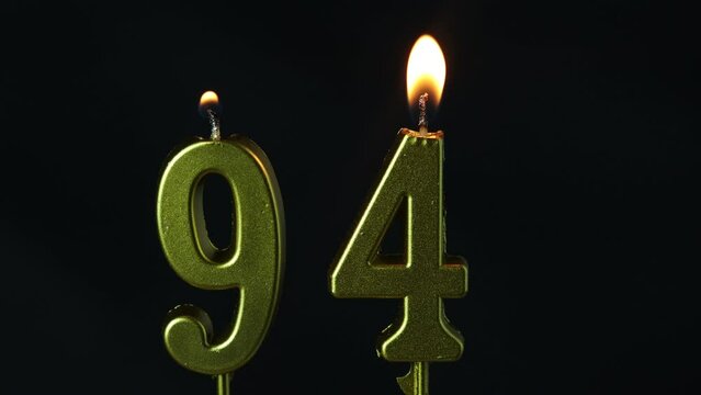 close up on gold number ninety-fourth birthday candle on a dark background.
