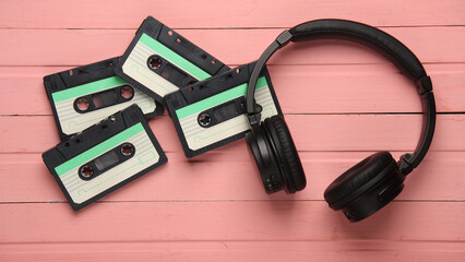 Retro 80s audio cassettes with stereo headphones on pink wooden boards. Top view