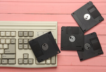 Retro floppy disks and old-fashioned keyboard on pink wooden boards. 80s technology. Top view