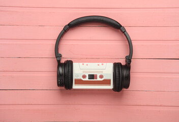 Retro 80s audio cassette with stereo headphones on pink wooden boards. Top view