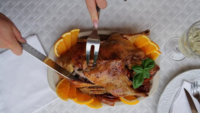 Baked duck goose stuffed apples on a platter, female hands cutting duck breast. Top view