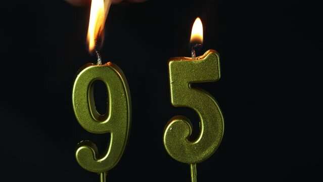 close up on gold number ninety-fifth birthday candle on a dark background.