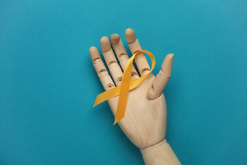 Yellow ribbon in wooden hand, childhood cancer awareness day symbol on blue background