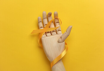 Yellow ribbon in wooden hand, childhood cancer awareness day symbol