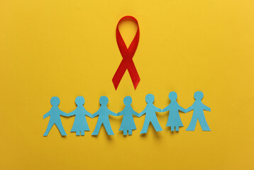 Red awareness ribbon with paper cut people chain on yellow background. Worlds HIV Aids Day