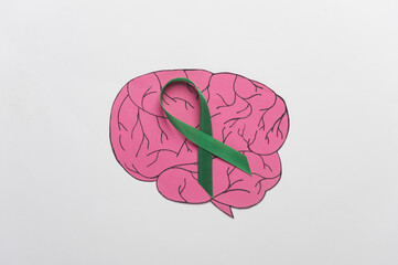 Green awareness ribbon with paper brain on white background. World mental health day concept