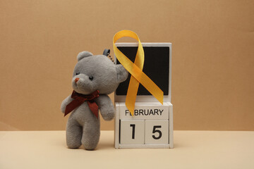 Yellow ribbon, calendar with date february 15 and Teddy bear. World childhood cancer awareness day