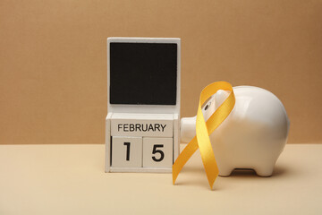 Yellow ribbon, calendar with date february 15 and piggy bank. World childhood cancer awareness day