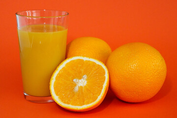 Glas of orange juice wirh oranges and cut open orange with orange background.