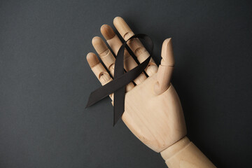 Black awareness mourning ribbon in wooden hand on dark background