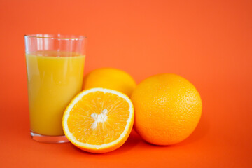 Glas of orange juice wirh oranges and cut open orange with orange background.