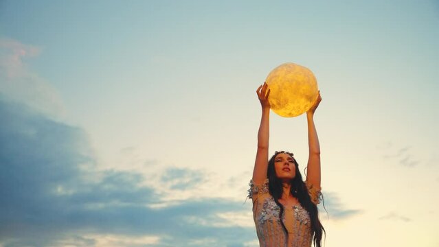 Fantasy woman holding moon magic light glowing planet in hands background evening dusk sky blue clouds heaven. Girl night elf beauty face, sexy dress dark sky lake. Lady fairy queen art fortune teller