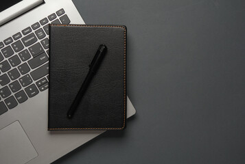 Laptop and Notebook with black leather cover, pen on dark gray background - obrazy, fototapety, plakaty