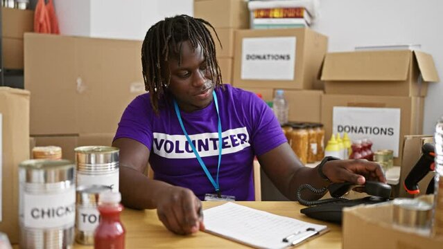 African american man volunteer talking on telephone writing on clipboard celebrating at charity center