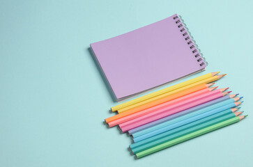 Set of colored pencils and notebook on a blue background