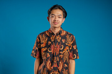 Young Asian man wearing batik shirt looking at the camera with confident expression isolated on blue background