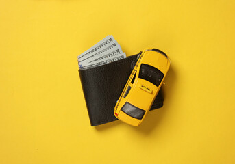 Toy taxi car model and purse with dollar bills on yellow background. Business concept. Top view