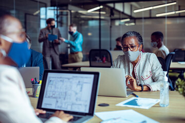 A focused woman working on her laptop in an office while wearing a face mask