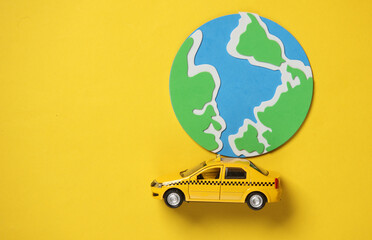 Toy taxi car model with globe on yellow background. Travel concept. Top view