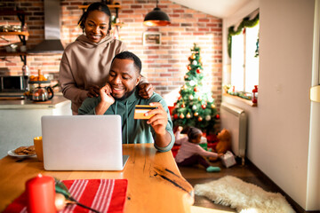 Happy young couple holding a credit card and looking at the laptop at home